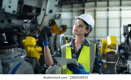 A female engineer installs a program on a robotics arm in a robot warehouse. And test the operation before sending the machine to the customer.