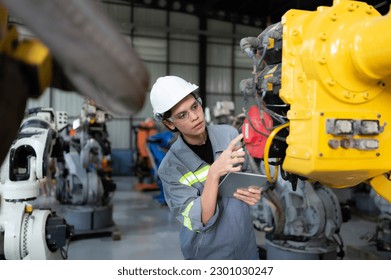 A female engineer installs a program on a robotics arm in a robot warehouse. And test the operation before sending the machine to the customer.