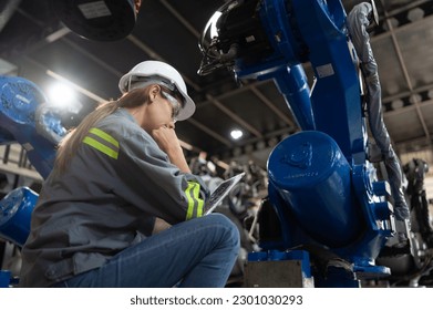 A female engineer installs a program on a robotics arm in a robot warehouse. And test the operation before sending the machine to the customer.