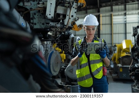 A female engineer installs a program on a robotics arm in a robot warehouse. And test the operation before sending the machine to the customer.
