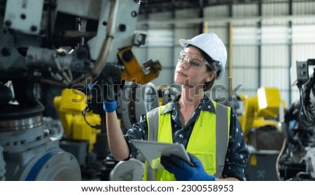 A female engineer installs a program on a robotics arm in a robot warehouse. And test the operation before sending the machine to the customer.