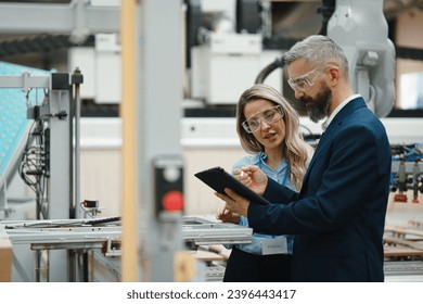 Female engineer and male production manager standing in modern industrial factory, talking about production. Manufacturing facility with robotics and automation. - Powered by Shutterstock