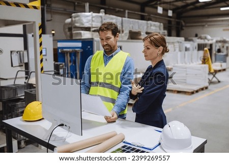 Female engineer reading technical documentation with project manager in modern industrial factory, talking about new production project, investment. Team management in manufacturing facility.