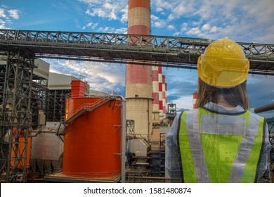 The female engineer was standing and wearing a safety hat and reflective jacket at the front, a flue gas mine and a coal conveyor.belt.