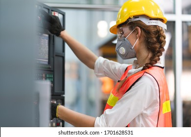 Female Engineer Wear Face Mask With Safety Vest And Yellow Helmet Operating Control CNC Machinery At Factory Industrial