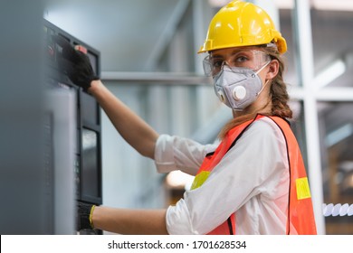 Female Engineer wear face mask with safety vest and yellow helmet operating control CNC Machinery at factory Industrial