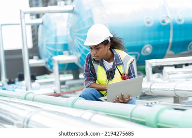 Female engineer work using laptop computer for checks or maintenance in sewer pipes area at construction site. African American woman engineer working in sewer pipes area at rooftop of building