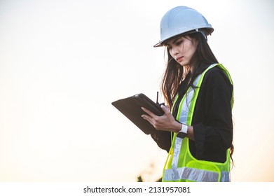 A female engineer is working on a job site and is using a tablet and carrying a walkie-talkie, She is wearing protective workwear and white helmet. - Powered by Shutterstock