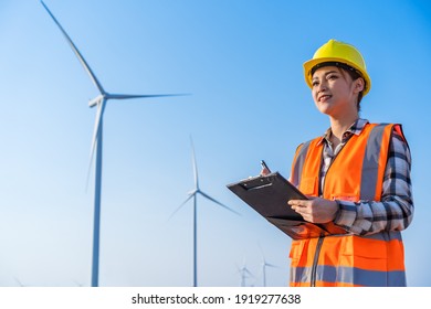 ingeniera femenina trabajando y escribiendo en un portapapeles contra la granja de turbinas eólicas