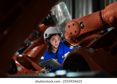 female engineer,technician wearing safety uniform use tablet to checking machine operation industrial robot, a robot system used for manufacturing. assembly of industrial parts using robotic arms - Powered by Shutterstock