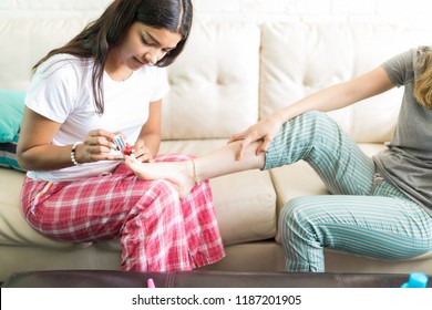 Female Enjoying Sleepover And Pampering Friend By Applying Nailpolish On Couch At Home