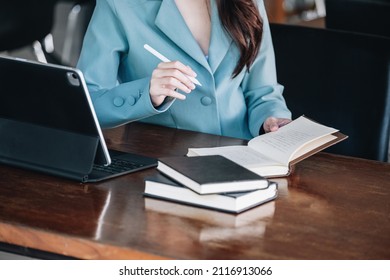 A Female Entrepreneur Or Businesswoman Showing A Smiling Face While Reading A Book Developing Financial And Investing Strategies And Operating A Computer Tablet Working On A Wooden Table