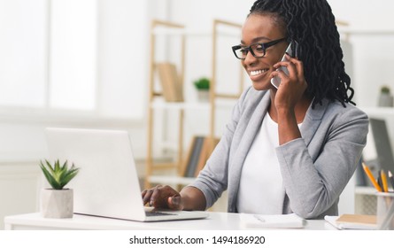 Female Entrepreneur. Cheerful African American Businesswoman Talking On Phone Working On Laptop In Modern Office. Empty Space - Powered by Shutterstock