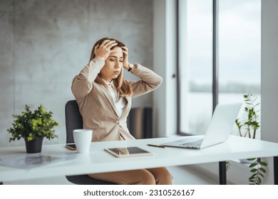 Female entrepreneur with headache sitting at desk. Businesswoman under terrible physical tension at work. Business woman with hands on her face looking exhausted - Shutterstock ID 2310526167