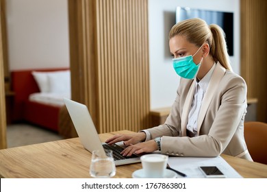 Female Entrepreneur With Protective Face Mask Typing An E-mail On A Computer In Hotel Room. 