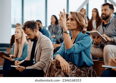 Female entrepreneur raising her hand to answer a question during business conference in convention center.  - Shutterstock ID 2346168353