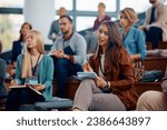 Female entrepreneur taking notes while attending a business seminar in conference hall.