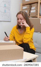Female entrepreneur taking notes while talking on mobile phone with customer and managing orders working in his small business store at home office. copy space