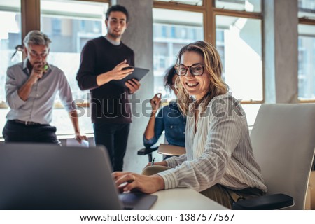 Female entrepreneur working on laptop and explaining strategy to attract followers to online web store while having meeting with colleagues in office.