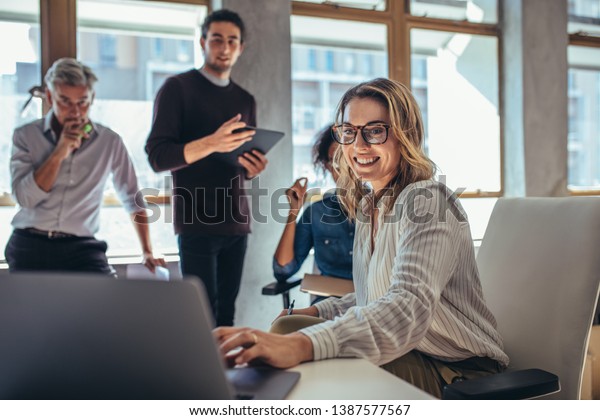 Female entrepreneur working on laptop and\
explaining strategy to attract followers to online web store while\
having meeting with colleagues in\
office.
