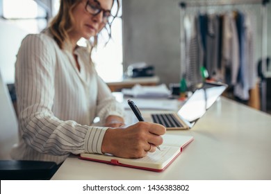 Female entrepreneur writing in her diary with laptop on desk. Online business owner working at her desk.