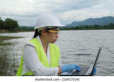 Female Environmentalist Wearing Gloves Takes Samples Of River Water To Examine Contaminants In Natural Waters And Record Data On A Laptop. Water And Ecology Concept.