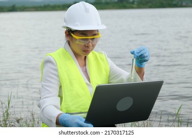 Female Environmentalist Wearing Gloves Takes Samples Of River Water To Examine Contaminants In Natural Waters And Record Data On A Laptop. Water And Ecology Concept.