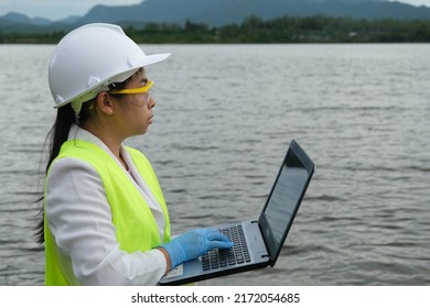 Female Environmentalist Wearing Gloves Takes Samples Of River Water To Examine Contaminants In Natural Waters And Record Data On A Laptop. Water And Ecology Concept.