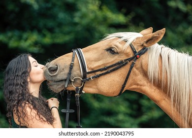 A female equestrian cuddles with her bridled kinsky horse. Portrait of a young woman giving a little kiss on her horses nose - Shutterstock ID 2190043795