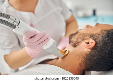 Female esthetician hands in sterile gloves removing unwanted hair from male neck with special laser device - Shutterstock ID 1820138045