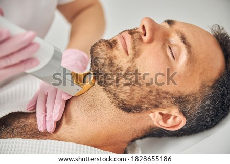 Female esthetician hands in sterile gloves removing unwanted hair from male neck with laser device