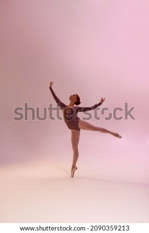 Female european ballerina dancing classical ballet dance. Choreography concept. Young pretty woman wear leotard and ballet shoes. Fit girl looking away on bright pink background in studio. Copy space