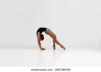 Female european ballet dancer dancing classical ballet dance. Choreography concept. Young flexible girl with red hair barefoot and wearing leotard. Isolated on white background in studio. Copy space