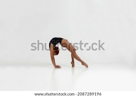 Female european ballet dancer dancing classical ballet dance. Choreography concept. Young flexible girl with red hair barefoot and wearing leotard. Isolated on white background in studio. Copy space