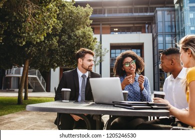 Female executive explaining new business strategy to team while sitting outdoors at table. Business professionals discussing work at office cafeteria. - Powered by Shutterstock