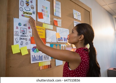 Female Executive Pointing The Document On Bulletin Board In Office