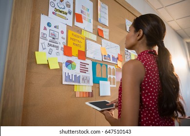 Female Executive Using Digital While Looking At The Bulletin Board In Office