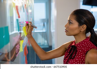 Female executive writing on glass board with a marker in office - Powered by Shutterstock