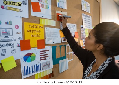 Female Executive Writing On Sticky Note At Bulletin Board In Office