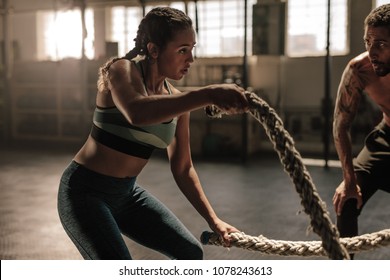 Female exercising with battle ropes at the gym with coach. Athlete doing battle rope workout at gym with trainer.