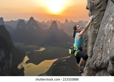 Female extreme climber conquers steep rock against the sunset over the river. China, typical Chinese landscape with mountains and river.
