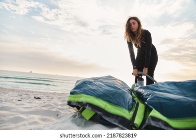 Female Extreme Sports Kite Surfer Prepping Kite On Beach During Sunset