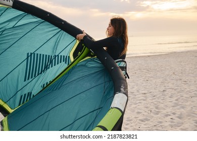 Female Extreme Sports Kite Surfer Prepping Kite On Beach During Sunset