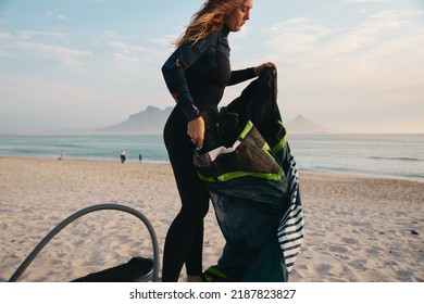 Female Extreme Sports Kite Surfer Prepping Kite On Beach During Sunset