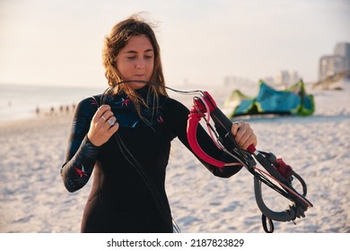 Female Extreme Sports Kite Surfer Prepping Kite On Beach During Sunset