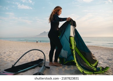 Female Extreme Sports Kite Surfer Prepping Kite On Beach During Sunset