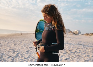 Female Extreme Sports Kite Surfer Prepping Kite On Beach During Sunset