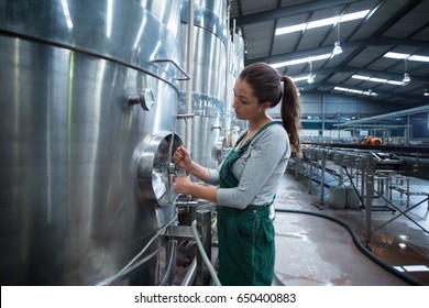 Female factory worker turning control wheel of storage tank at drinks production factory - Powered by Shutterstock