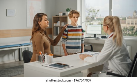 Female Family Doctor Talking With Young Pregnant Woman And Her Teenage Boy During Consultation In A Health Clinic. Experienced Physician In Lab Coat Sitting Behind A Computer Desk In Hospital Office.