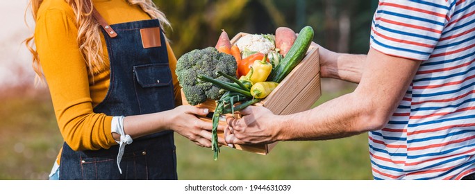 Female farmer giving box of veg to customer on a sunny day. Farmer giving box of veg to customer on a sunny day. Local farmer talks with customer at farmers' market - Powered by Shutterstock